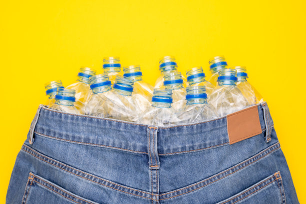 塑料瓶回收技术制作衣服。俯视图旧水瓶和蓝色短裤牛仔裤上的黄色图片下载