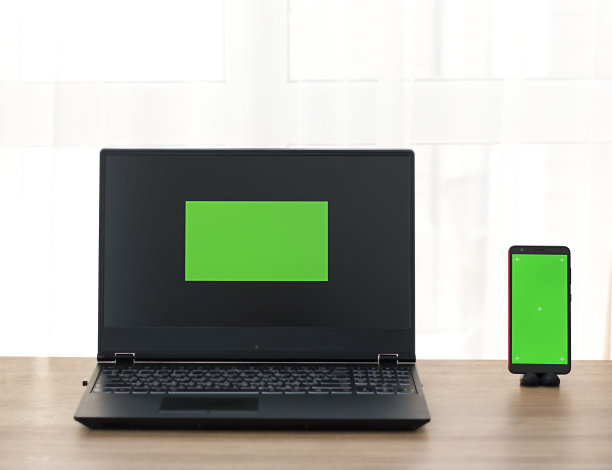 Chromakey。笔记本电脑和手机，绿色屏幕放在家里的木制桌子上。图片下载