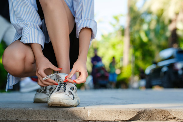 身穿条纹衬衫的黑发千禧女性站在城市公园，户外系鞋带跑步鞋准备跑步。女生慢跑锻炼动机健康健身。图片下载