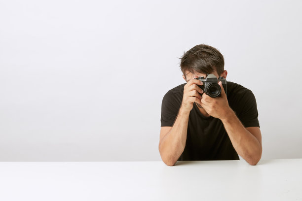 白人青年在白底照相馆的照相机前用模拟照相机拍照图片下载
