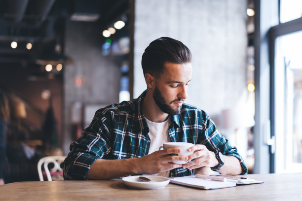 专注的年轻胡子阅读笔记本和喝咖啡在阁楼咖啡馆图片下载