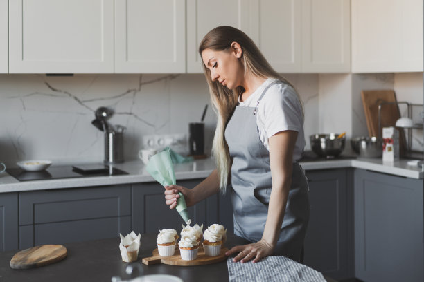 年轻可爱的女糕点师在家用生奶油装饰小蛋糕图片下载