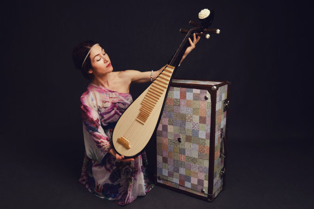 一个快乐的女音乐家穿着亚洲服装在工作室的黑色背景。黑色的背景上是一个微笑的女人，手里拿着来自亚洲的弦乐器图片下载