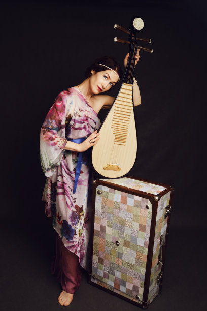 一个快乐的女音乐家穿着亚洲服装在工作室的黑色背景。黑色的背景上是一个微笑的女人，手里拿着来自亚洲的弦乐器图片下载