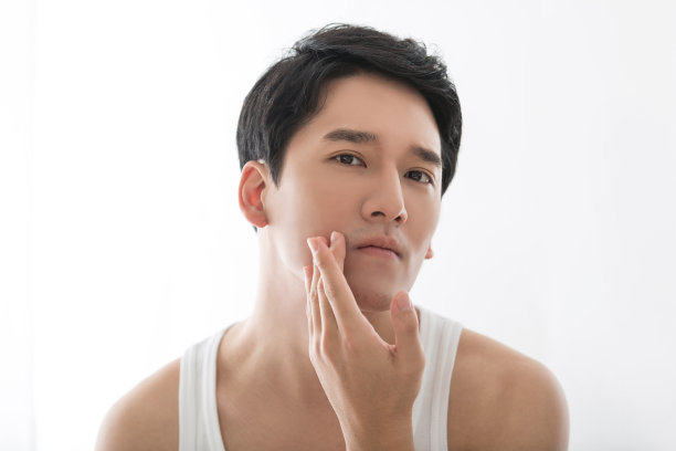 英俊的年轻东亚男子检查他的下巴，胡子和皮肤在镜子库存的照片图片下载