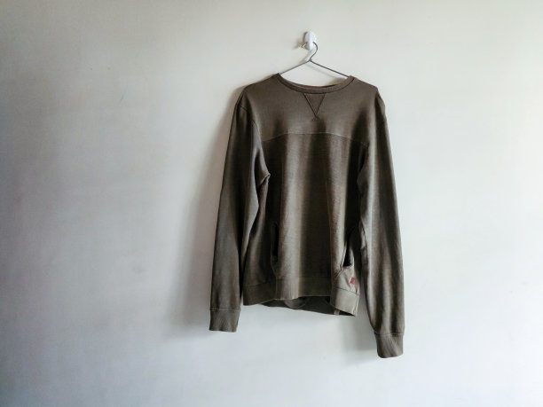 军绿色男士全袖t恤库存照片，用钢衣架挂在浅黄色油漆的墙上。这张照片是在泰伦加纳海得拉巴自然光下拍摄的。有选择性的重点。图片下载