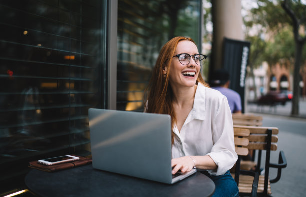 快乐的女人在咖啡馆外使用笔记本电脑图片下载