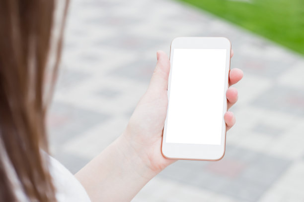 一名女子拿着一部白色智能手机，背景是城市街道的黑屏，背影图片下载