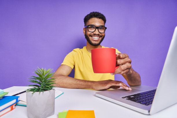 英俊的非洲男子拿着杯子，坐在桌子上的紫色背景图片下载