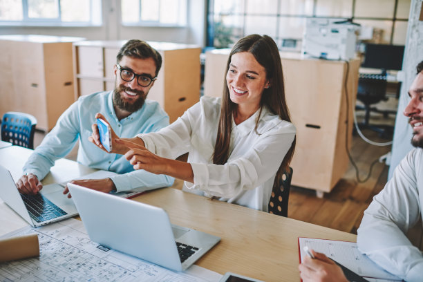 快乐的男女同事在室内通过手机的前置摄像头一起自拍，快乐的成功伴侣在办公室休息时用智能手机拍照图片下载