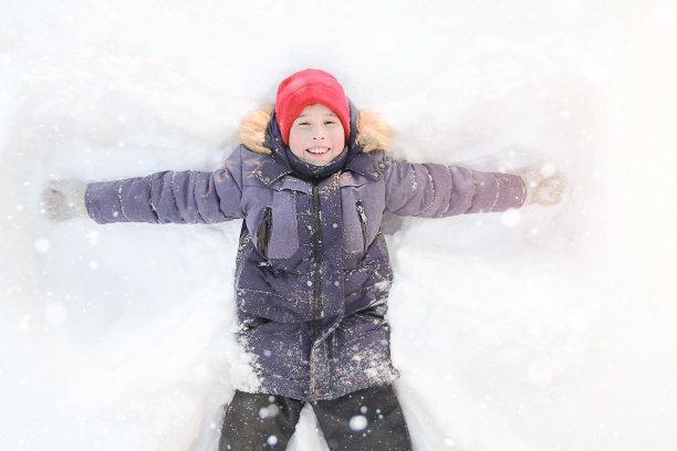 快乐，快乐的男孩躺在雪地上笑。冬季概念在街头游戏，孩子们在冬天休息。快乐的孩子做一个雪天使图片下载