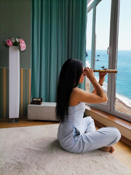 一个年轻的女人透过一个旧的望远镜透过窗户看着海浪图片下载