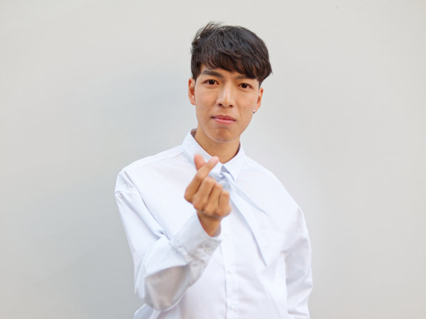 白衬衫黑发的中国青年男子肖像，在白色背景前摆姿势，手指比心，正面视角图片下载