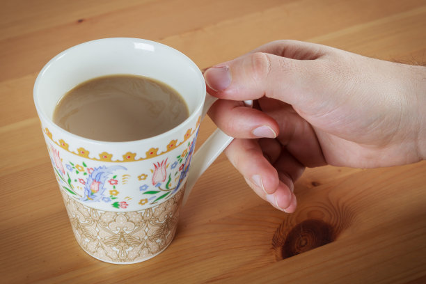 年轻的白人男子手拿咖啡与牛奶在图案杯在木制桌子的背景图片下载
