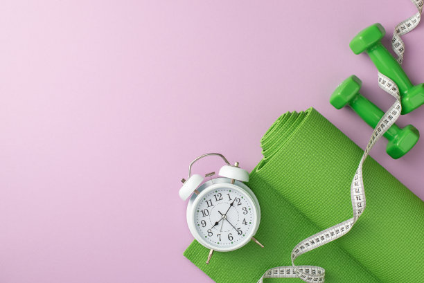 体育的概念。俯视图照片的绿色运动垫卷尺测量哑铃和闹钟上孤立的淡紫色背景图片下载