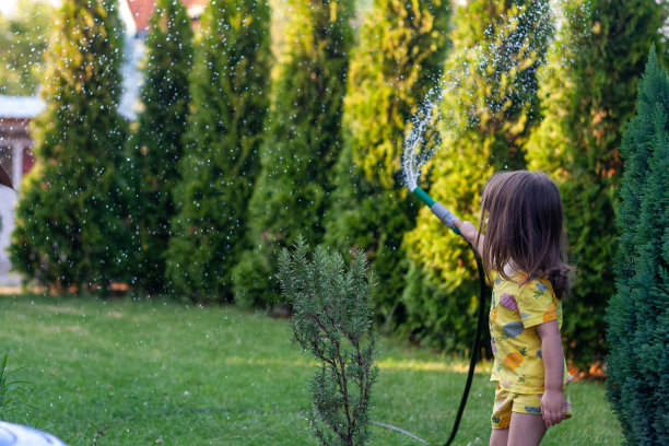 这个小女孩正在用水管在草地上浇水。图片下载