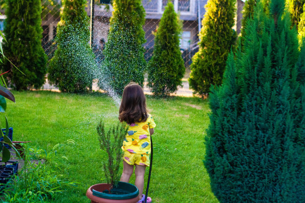 这个小女孩喜欢晴天。她给后院的草浇水。图片下载