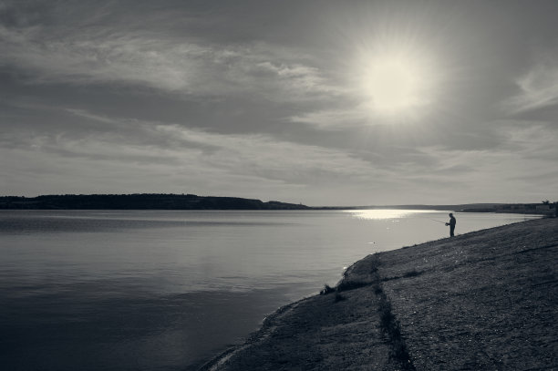 一个大湖在夕阳的照耀下，在铺满混凝土板的岸边，一个孤独的渔夫站在那里捕鱼图片下载