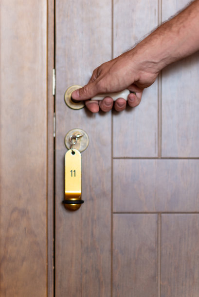 一个男人的手放在一个木制的酒店门的把手上，钥匙链上有11号。图片下载