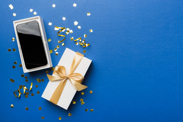 打开礼品盒，金色丝带和智能手机彩色背景，俯视图。空白开箱包装模型，模板为您的设计品牌模型图片下载