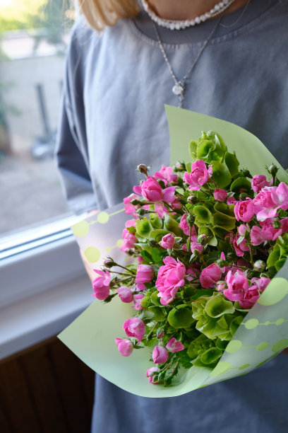 一束粉红色美丽的玫瑰在一个女人的手中。花店老板手中时髦的鲜花。这个女孩收了一束粉红色和绿色的鲜花。美丽的花朵图片下载