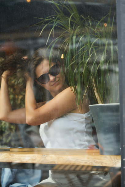 一个穿着白色t恤的女孩坐在咖啡馆里，透过玻璃看风景图片下载