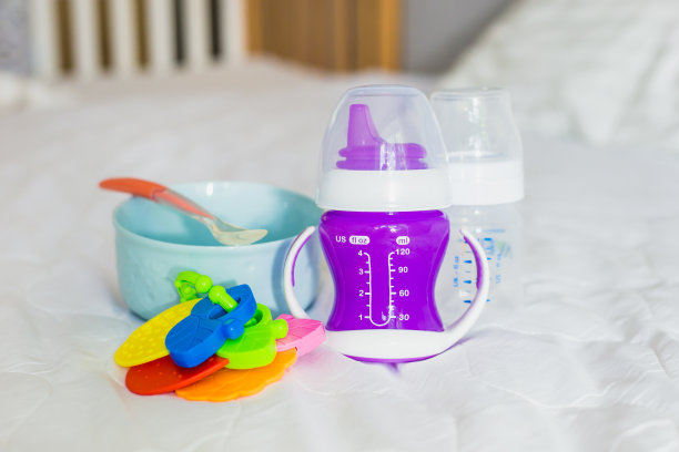 白色的床上放着一套婴儿餐具。盘子，勺子，盛水的瓶子放在床单上。婴儿喂养、食物图片下载