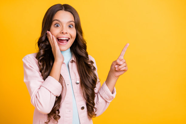 照片迷人的棕色卷发小女孩点copyspace手脸颊穿粉红色夹克孤立在黄色的颜色背景图片下载