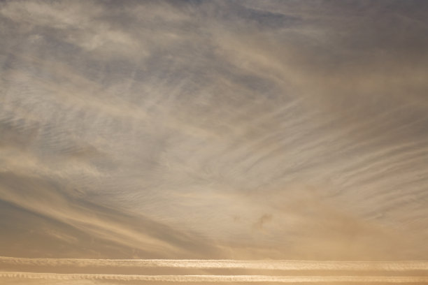 夕阳西下的天空，云朵被太阳照亮。尾迹和羽状云。图片下载