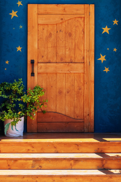 有阳光照耀的台阶的红木门廊，一盆植物靠在一堵有金色星星的蓝色墙壁上。公园的照片。前视图。图片下载