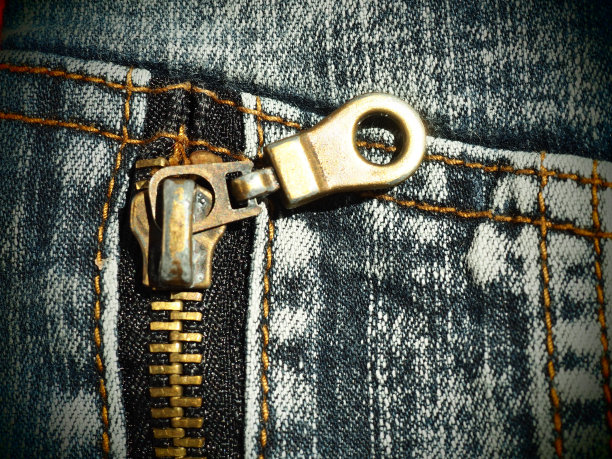 特写牛仔布与接缝和锁。破旧不堪的牛仔裤金属青铜黄色带转轮锁紧。垂直接缝。图片下载