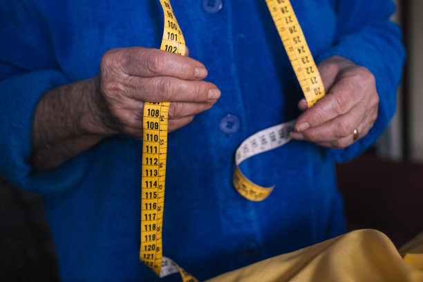 老奶奶退休后在家里做裁缝，手里拿着卷尺。图片下载