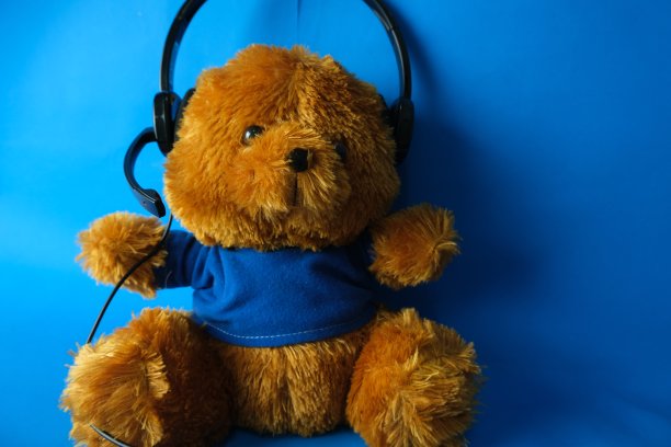 棕色的泰迪熊戴着蓝色背景的耳机图片下载