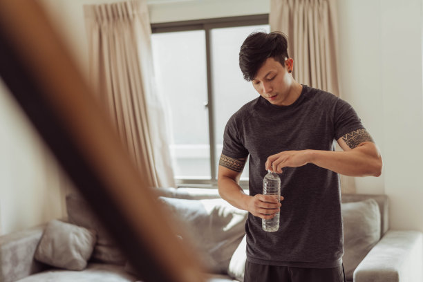 健康的男人喝水，休息一下，在家锻炼。年轻的亚洲男子在家锻炼后休息。图片下载