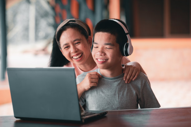 残疾青年在轮椅上与母亲一起使用电脑，在家上学的概念。图片下载