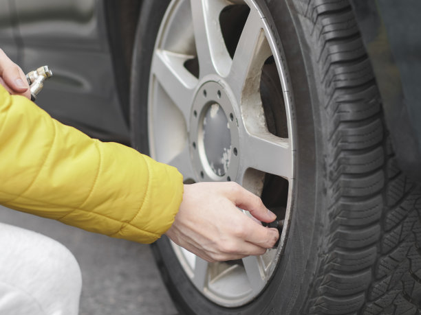 穿着黄色夹克的年轻白人男子的手在一辆汽车肮脏的后轮上转动线轴的尖端图片下载
