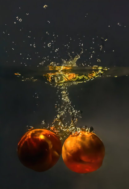 两个桃子扔进水里溅起阵阵气泡。暗的背景图片下载
