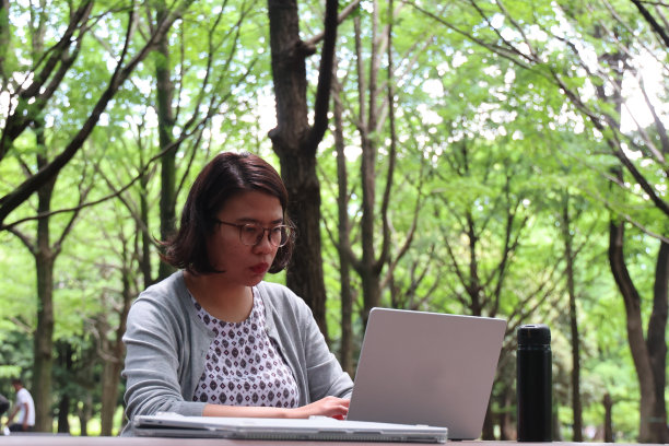 一个年轻女子坐在公园的户外，手里拿着一台笔记本电脑图片下载