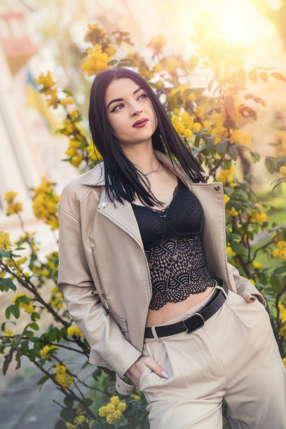 穿着白色皮夹克的时髦女人在春天花园的樱花附近摆姿势图片下载