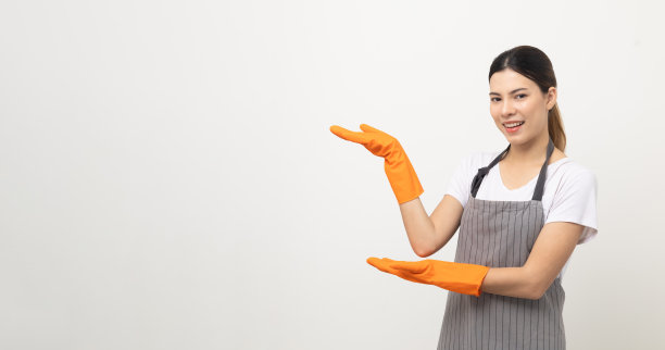 年轻美丽的女人与围裙和橡胶手套站在开放的双手手掌向上孤立的白色背景。家政家务或女佣的概念。图片下载