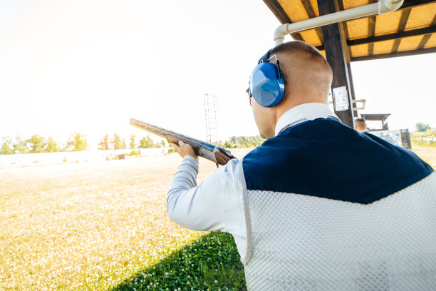 成年男子戴着墨镜，戴着防护耳机，穿着步枪背心练习射击。图片下载