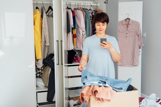 一名妇女用她的智能手机拍下短裤的照片，用于出售或捐赠她的衣服。整理，整理衣服，整理衣柜。重用,二手的概念。意识的消费者。图片下载