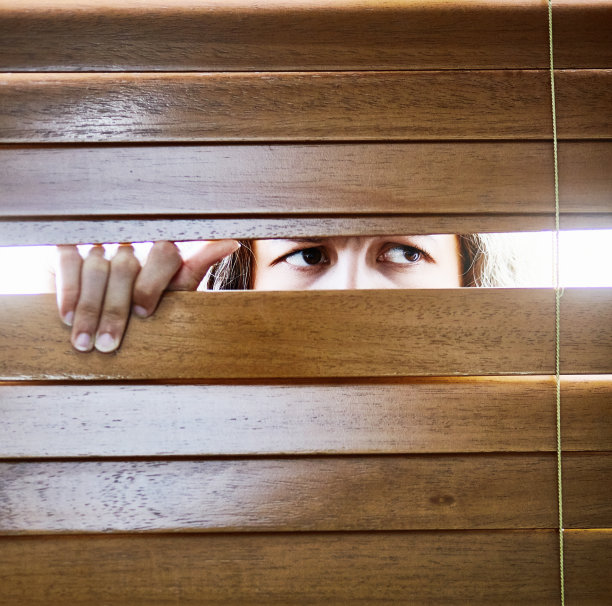 焦虑的年轻女子偷偷地透过百叶窗看图片下载