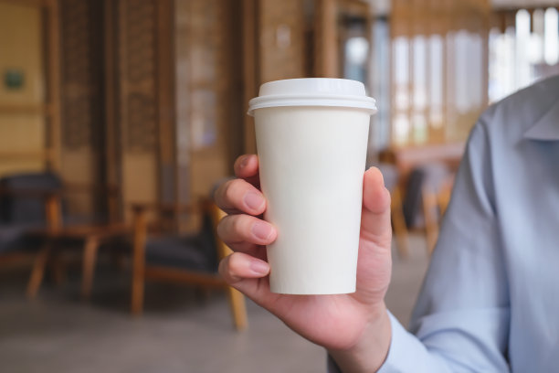 在咖啡馆里，男人手捧着一杯热咖啡。带走热饮。图片下载