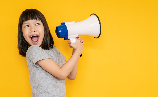 年轻有趣的肖像聪明快乐的小亚洲女孩孤立在黄色工作室拍摄。教育面向小学幼儿园，小女孩拿着扩音器回到学校的理念。图片下载