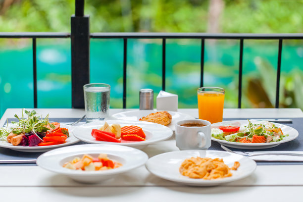 在豪华热带酒店或度假村的户外餐厅露台上提供早餐。提供食物和饮料的早午餐餐桌。暑假、假期、旅游、旅游概念。绿色的池塘背景图片下载