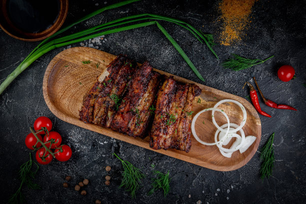 黑石桌上放着烤排骨，还有蔬菜、奶油和番茄酱。放在木板上的。快餐店，外卖服务。图片下载
