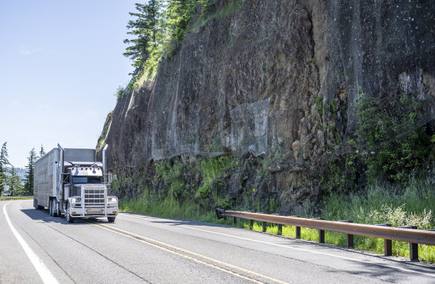 黑色经典的美式大型半挂车，带格栅护栅和铬合金零件，载着动物半挂车行驶在蜿蜒的山路上图片下载