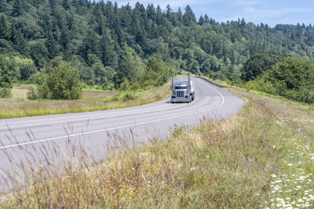 工业经典的大钻机半挂车牵引车，在蜿蜒狭窄的高速公路上用平板半挂车运输有盖货物图片下载