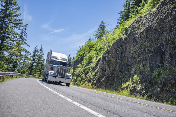 重型大钻机半挂车和干厢式半挂车行驶在弯弯曲曲的山间高速公路上，路旁有岩石和树木图片下载